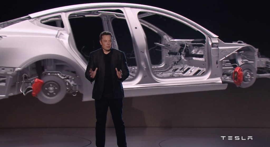 This screenshot from Tesla videos shows a rendering of the Tesla Model 3 body-in-white behind CEO Elon Musk. (Screenshot from Tesla video)