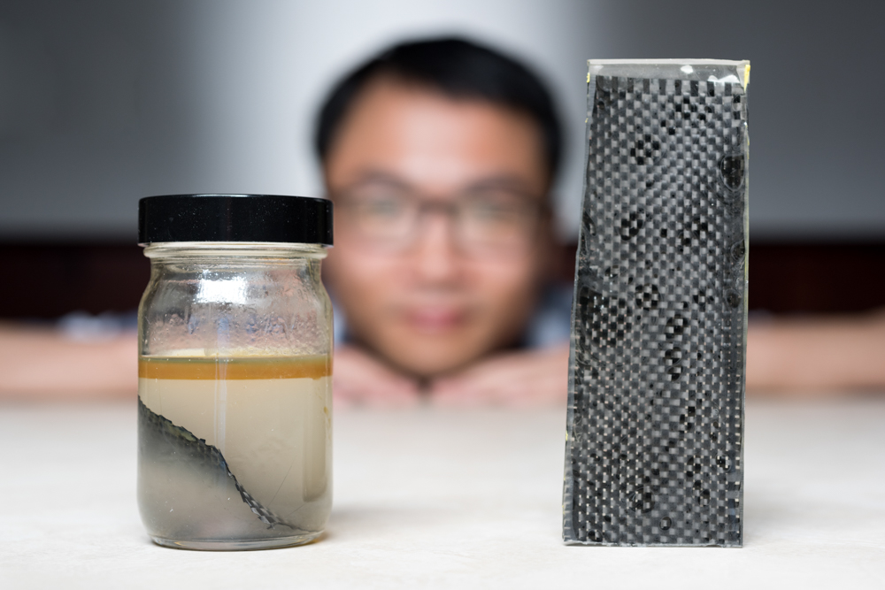 Kai Yu, a former postdoctoral researcher in The George W. Woodruff School of Mechanical Engineering at Georgia Tec, sits behind a piece of carbon fiber composite immersed in alcohol. (Rob Felt/Georgia Tech)